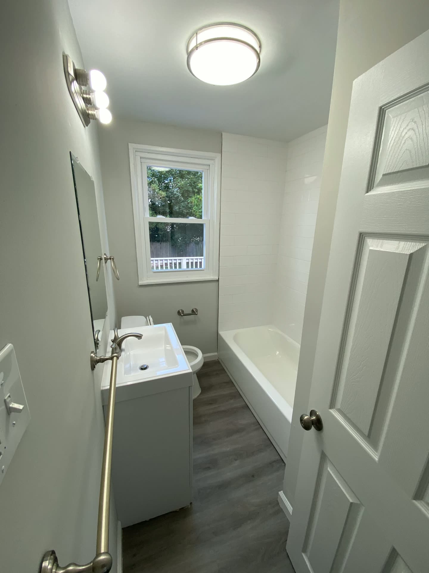 Baño renovado con azulejo blanco, vanidad nueva y piso tipo madera